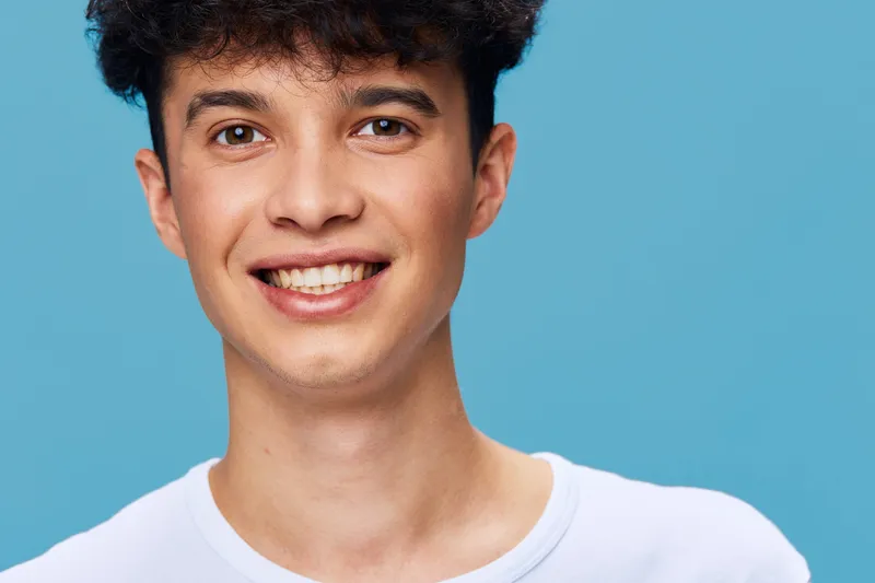 smiling man with curly hair wearing white t-shirt, blue background, youthful, casual style, close-up portrait with natural light, happy expression