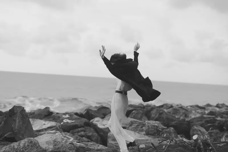 celebration, freedom, joy, embrace, outdoor, sea, rocks, shoreline, wind, movement, two figures on a windy coast celebrate a moment of release, a dramatic black and white scene capturing motion,