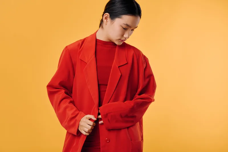 Woman in red coat and sweater looking down against yellow background, fashion portrait with modern style and casual confident pose for autumn or winter season.