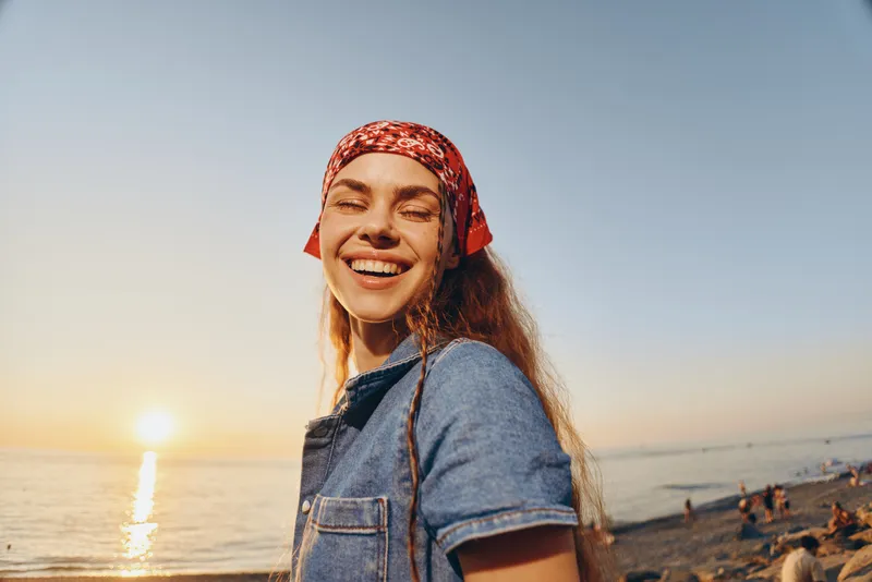 lifestyle woman wearing modern boho-western denim street style smiling at sunset, enjoying relaxed beach atmosphere, film color tone, warm natural light