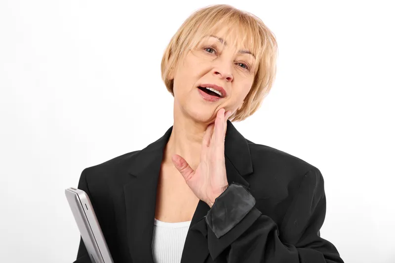 Older woman holding tablet, surprised expression, business portrait, thinking gesture with hand near chin, studio lighting on white background, communication moment