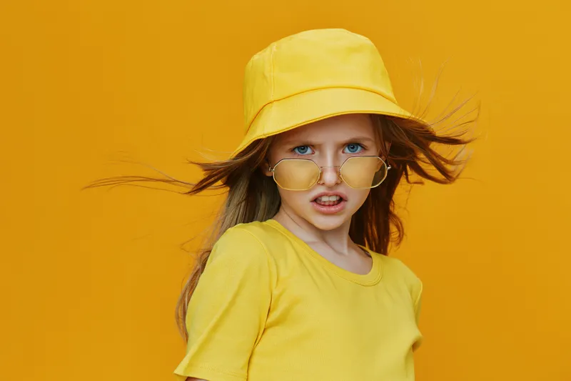 Playful girl with yellow hat and sunglasses against a bright yellow background, exuding confidence and joy, perfect for summer fashion themes