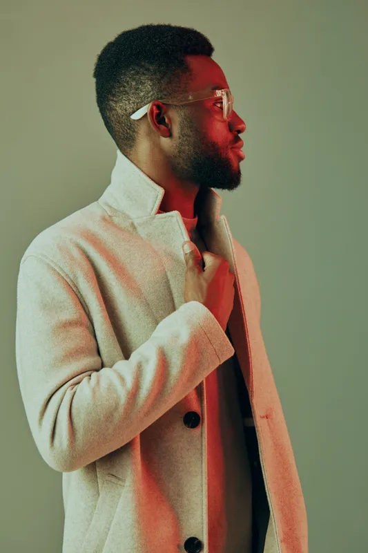 Stylish young man in a beige coat with glasses, showcasing confidence and elegance against a soft green backdrop, perfect for seasonal fashion concepts