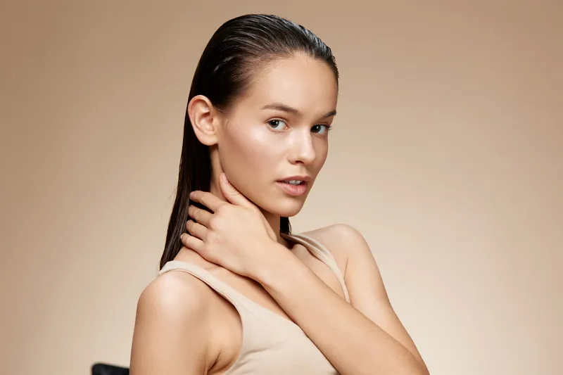 Young woman with wet hair poses confidently, showcasing her natural beauty and elegance against a soft beige background, ideal for beauty and skincare themes