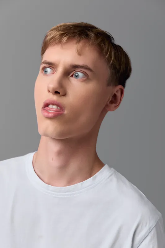 Man with surprise expression wearing a white tshirt in studio, looking to the side, isolated gray background, candid moment of curiosity and emotion, clean lighting and minimalist setup