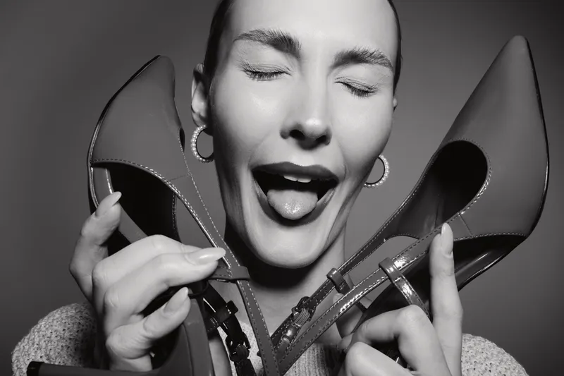 Close-up of a happy white woman with light skin holding a pair of high heel shoes near her face, eyes closed, expressing joy and excitement. Concept of fashion and lifestyle.