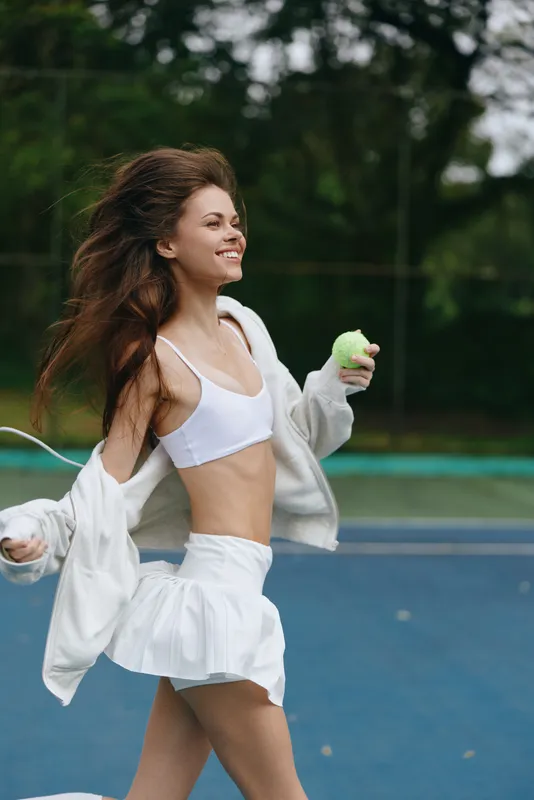 Young athletic woman in white sportswear enjoying a sunny day while playing tennis, showcasing happiness and energy on the court