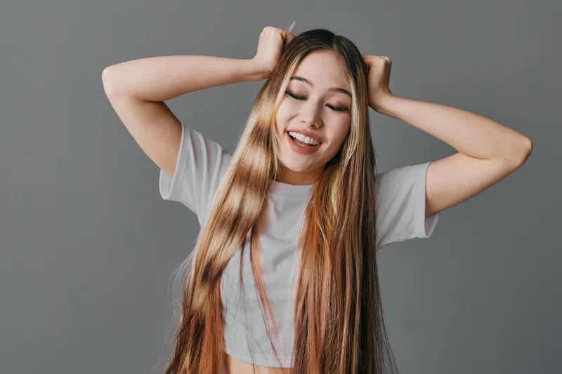 Young woman with long braided hair smiling with closed eyes and hands on head against grey background. Casual t shirt, happy face and relaxed pose with natural beauty.