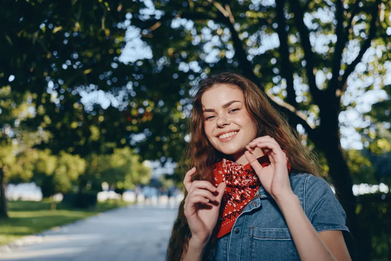 lifestyle woman in modern boho-western denim street style smiling outdoors with film color effect in natural park background on sunny day