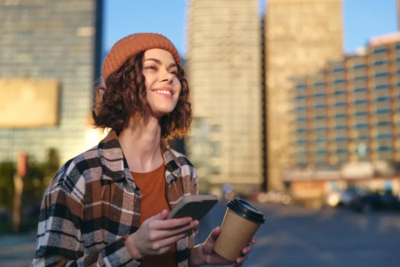 woman coffee smartphone city smile golden candid authenticity young woman in beanie and flannel holds takeaway cup and phone, enjoying golden hour glow with candid lifestyle, mindful living and