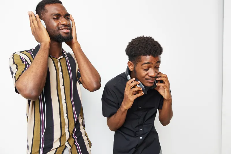 Two African American men enjoying music, expressing joy and excitement. They wear stylish outfits, with a vibrant atmosphere surrounding them.