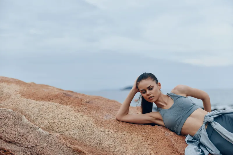 Young athletic model in sportswear relaxing on rocky beach, capturing the essence of fitness, serenity, and tranquility in a natural coastal setting