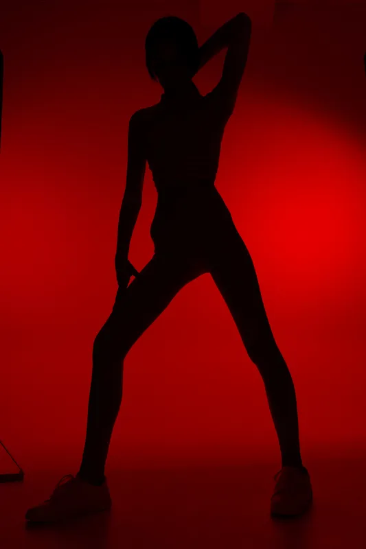 Silhouette of a woman sport fitness figure in dynamic pose with red backlight, highlighting athletic shape, strength, and active lifestyle in a dramatic studio setting.