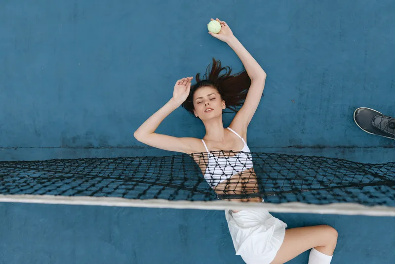 Young female athlete in sporty attire on a tennis court, expressing determination while holding a tennis ball, showcasing a vibrant blue background
