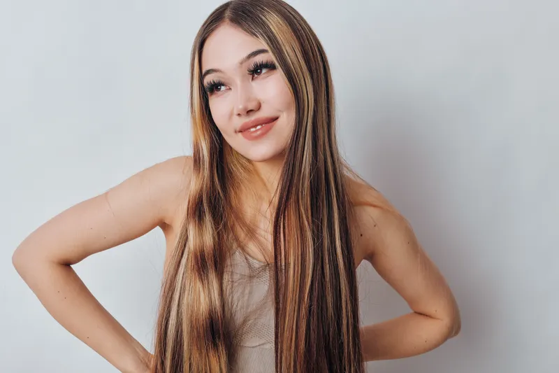 Young woman with long braided hair posing and smiling against light background, casual style, natural makeup and confident expression in studio portrait photography.