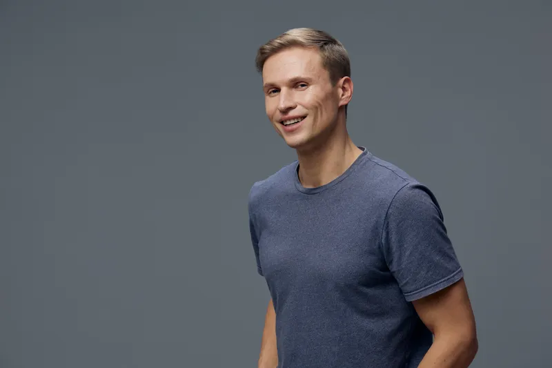 smiling young man wearing casual blue t-shirt standing isolated on gray background with positive facial expression digital nomad concept