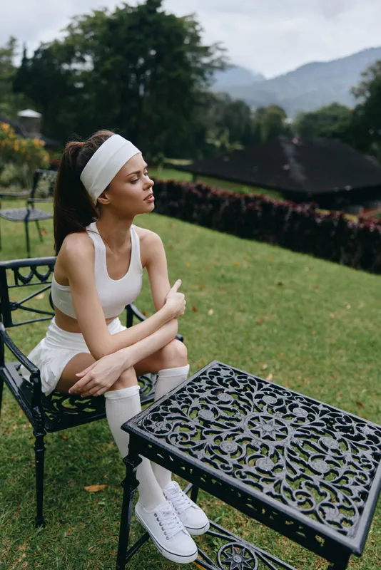 A young woman in athletic wear poses thoughtfully in a garden, showcasing a serene expression and a healthy lifestyle concept
