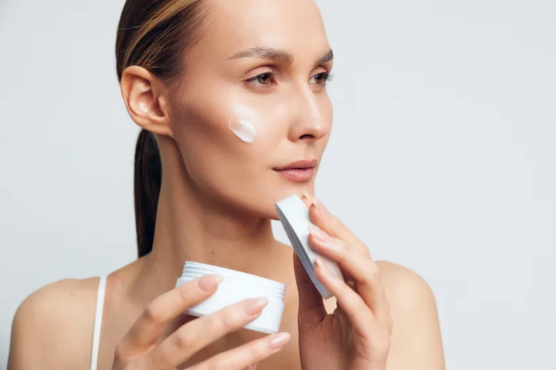 A young woman applies moisturizing cream as part of a skincare routine, with soft lighting and clean background, emphasizing hydration, glow, beauty and self care.