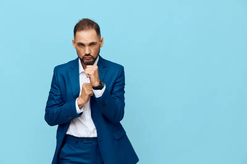Professional business man stands against a solid blue background, presenting a focused pose with a thoughtful expression. Isolated color backdrop enhances corporate style and emotion. The composition