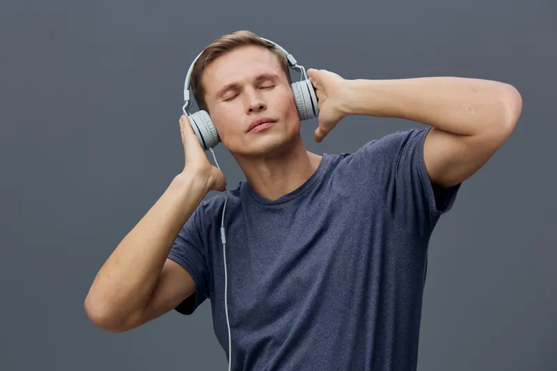 Relaxed young caucasian man in casual t-shirt wearing headphones listen to music close eyes isolated on gray background mental health and gadgets concept