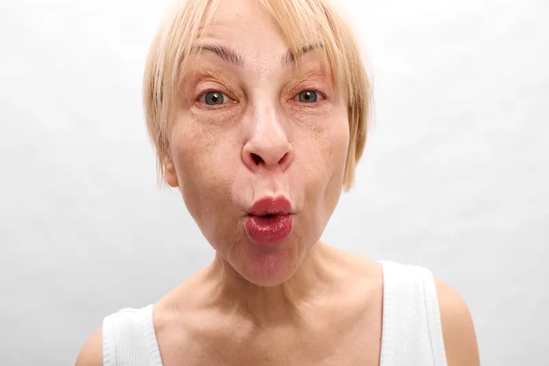 Woman surprised shocked closeup portrait of blonde young adult in studio lighting, open mouth and wide eyes, emotional face expression, soft minimal gray background, breathless mood