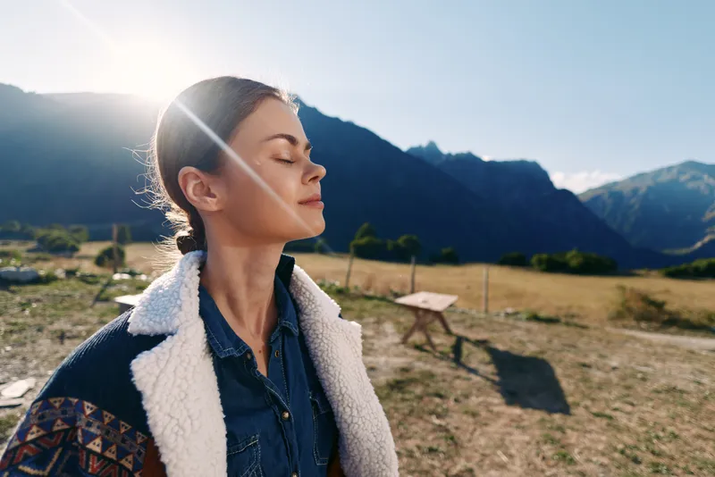 Woman profile with eyes closed in sun and mountains, outdoor nature portrait capturing relaxation and travel mood, peaceful breathing, scenic valley and warm light on face.