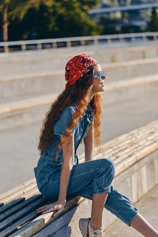 lifestyle woman wearing modern boho-western denim outfit with red bandana sitting outdoors in street style film color sunlight