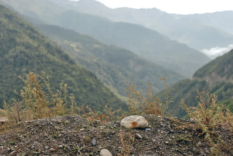 Stunning mountain landscape with rugged foreground rocks and distant misty peaks, capturing serene nature and expansive valley under a soft sky, inviting exploration and peaceful contemplation in the