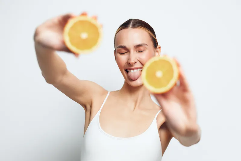 Smiling woman holding orange citrus, skincare wellness self care concept, studio lighting, close up portrait on white background, fresh vitamin for beauty, natural spa mood, morning glow
