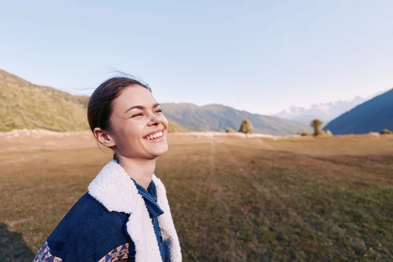 Woman smile portrait mountains meadow nature outdoor happiness captured in candid closeup of young female wearing fleece jacket at sunrise in scenic valley landscape enjoying freedom.
