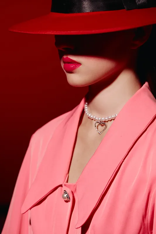 Portrait of a woman wearing a red hat casting shadows on her face with bright pink lipstick and a pearl necklace. Fashion creative beauty concept with dramatic lighting.