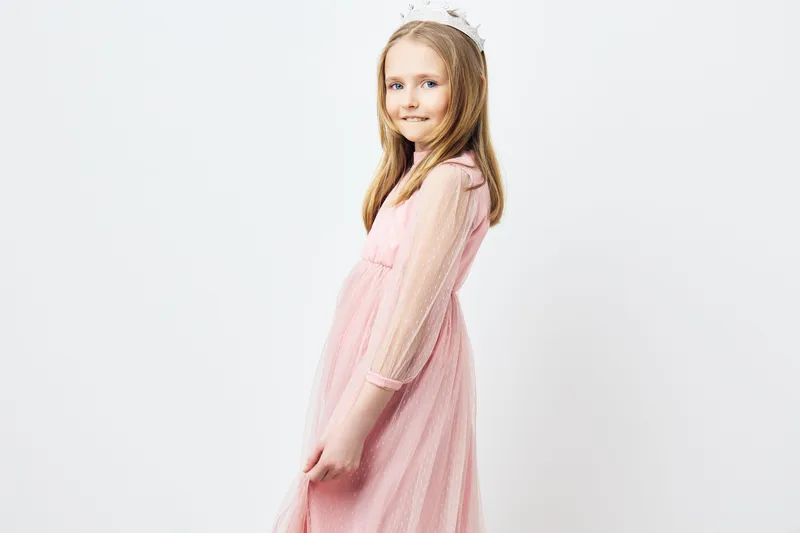 A cheerful young girl in a pink dress with a playful smile, showcasing joy and innocence against a soft, minimalist background, perfect for family themed projects