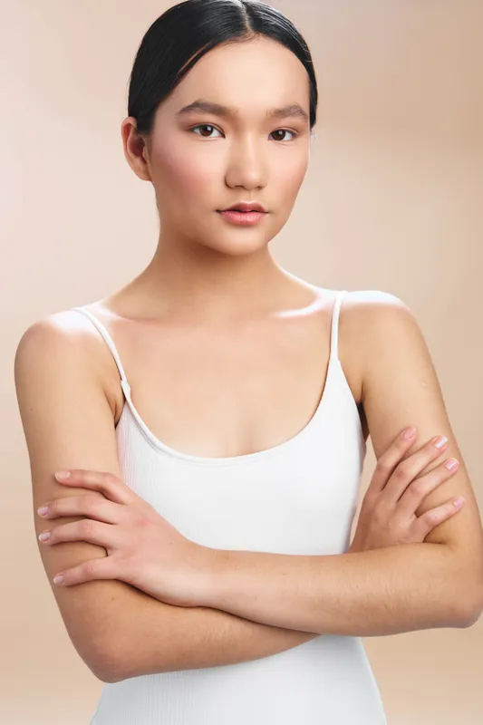 asian woman stands with arms crossed in a clean studio setting, calm expression, soft lighting, and minimalist backdrop, conveying confidence, poise, and contemporary professionalism.