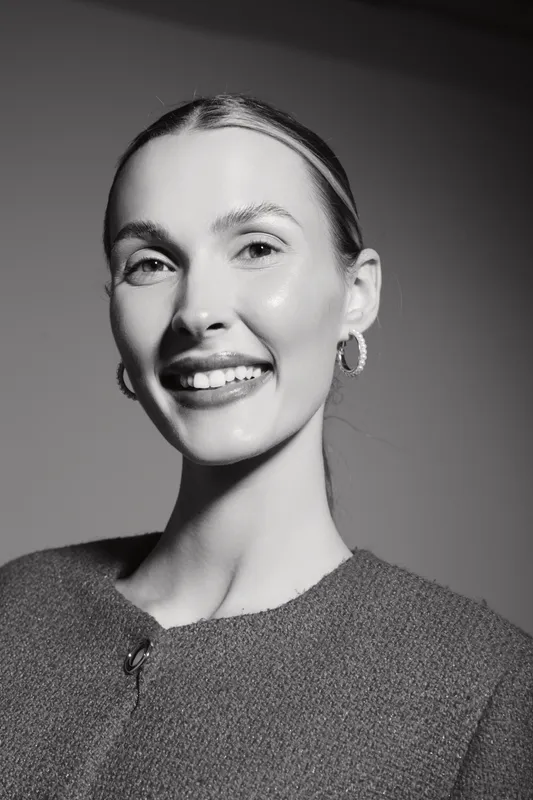 Smiling white woman with blonde hair in wool sweater looks happy in studio portrait with soft lighting and neutral background.