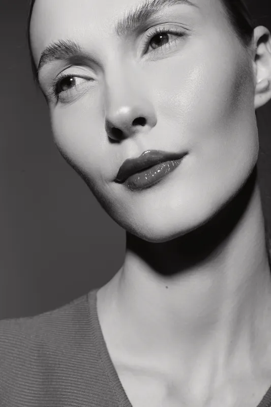 Close-up portrait of a young Caucasian woman with fair skin looking sideways. Soft lighting highlights natural facial features and smooth skin texture on a dark background.
