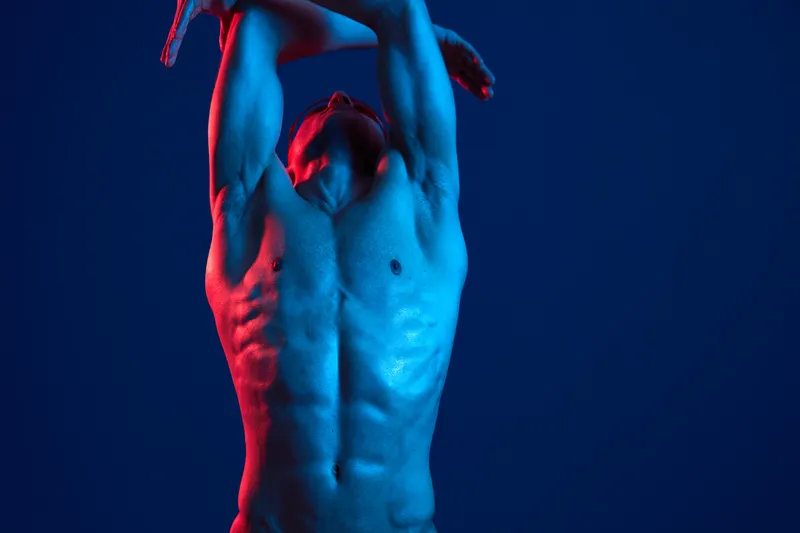 A muscular man showcasing his physical strength against a vibrant blue background, illuminated with striking red and blue hues. This captivating image emphasizes body art.