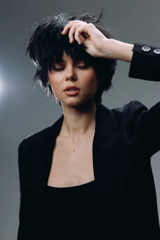 Young woman with short dark hair posing in black jacket, stylish and moody portrait, fashion and beauty concept