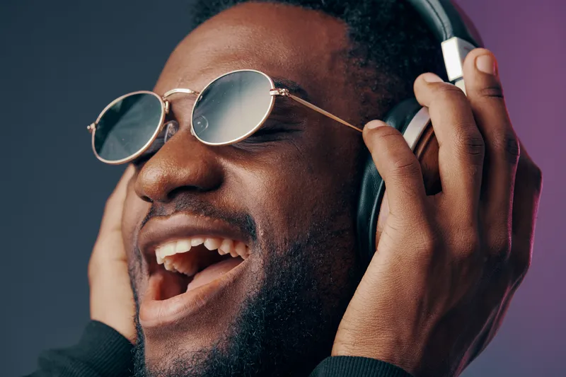 Joyful African man enjoying music with headphones and sunglasses against a vibrant backdrop, showcasing happiness and relaxation while listening to favorite tunes