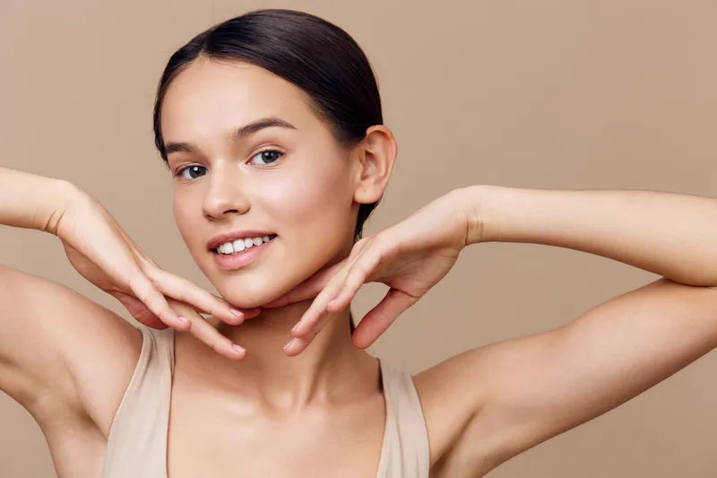 Young model with clear skin smiling softly, displaying skincare and beauty, with neutral tones and a minimalist background for wellness and confidence concepts
