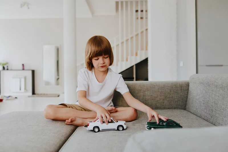Young boy playing with toy cars on a cozy couch, engaging in imaginative play while surrounded by a modern interior design, fostering creativity and joy.