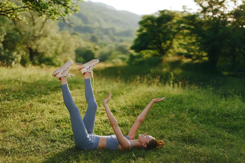 Young woman practicing yoga outdoors in a serene green landscape, wearing athletic wear and enjoying the moment with a joyful expression