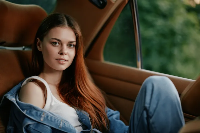 Young woman in casual denim outfit sitting in a car, showcasing natural beauty and relaxed emotions, with a beautiful green background.