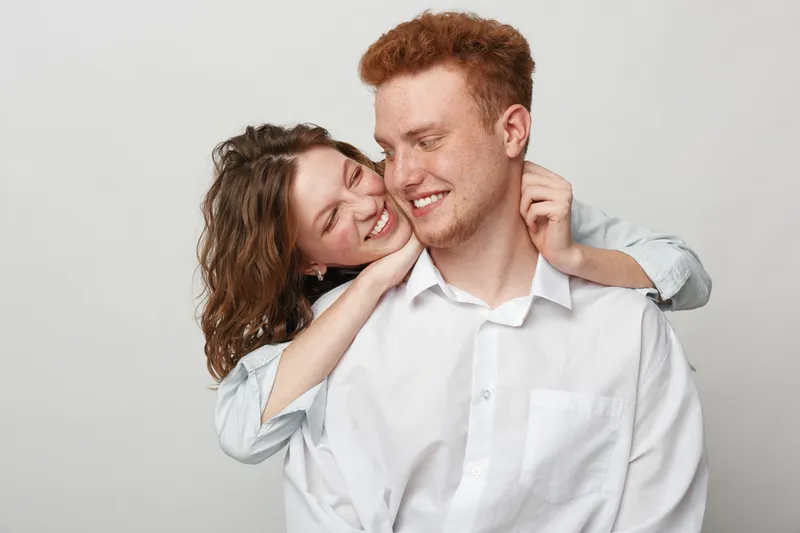 Happy young couple embraces and smiles in casual clothes on white background. Concept of love, relationship, friendship, happiness, and togetherness in studio portrait.