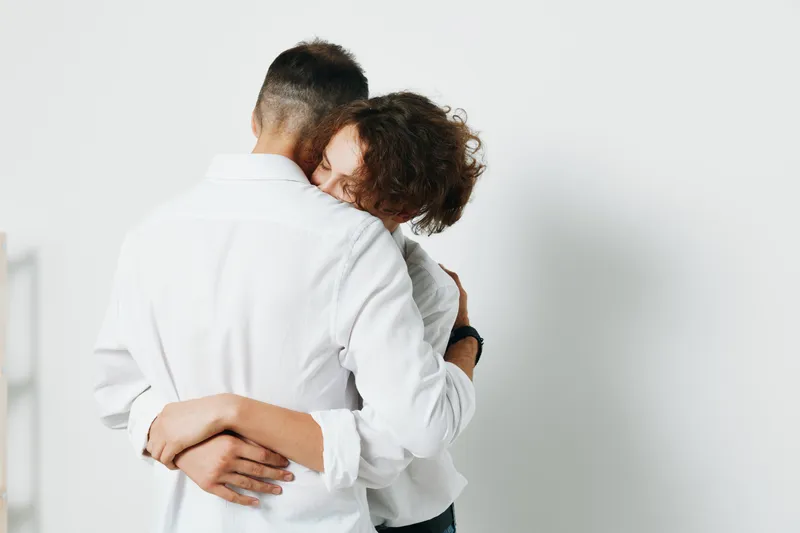 A professional man shares a warm embrace with a colleague against a solid colored background, conveying confidence, support, and determination in a business setting.