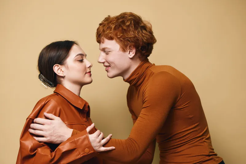 Couple, young man and woman embracing gently with loving expression on beige background. Intimate moment showing affection, connection and closeness between two people.