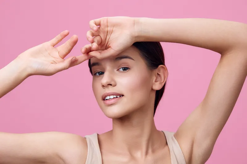 Young woman with a cheerful expression, posing against a pink background in a light outfit, showcasing beauty and confidence with a focus on skincare and health
