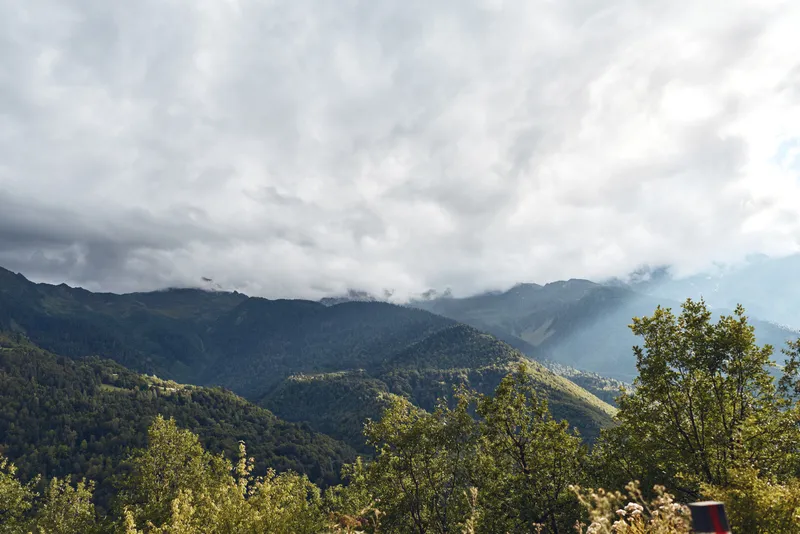 mountains forest clouds landscape mist sky trees hills under dramatic cloudy sky with layered mountain ridges and sunlight