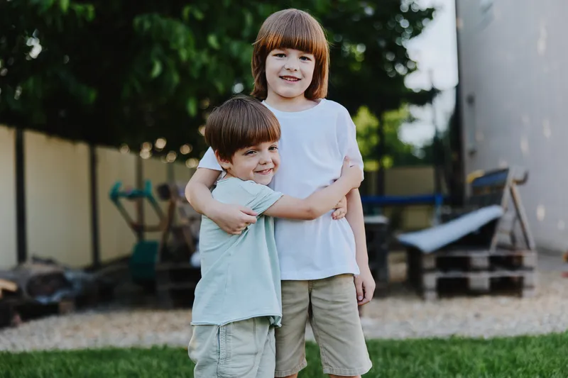 Two smiling boys embrace each other in a sunny backyard, showcasing their joy and playfulness. Perfect for family-oriented themes and childhood moments.