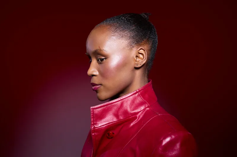 Profile of a confident dark skinned African woman wearing a red leather jacket against a red background. Concept for fashion, beauty, portrait, and empowerment of black women.