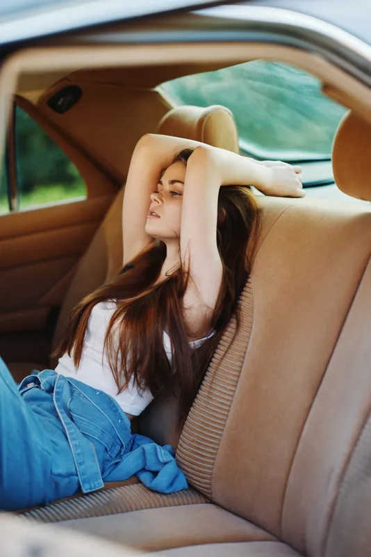Young woman relaxing in a car, showcasing casual fashion and natural beauty, surrounded by greenery. Her expression reflects serenity and peace.
